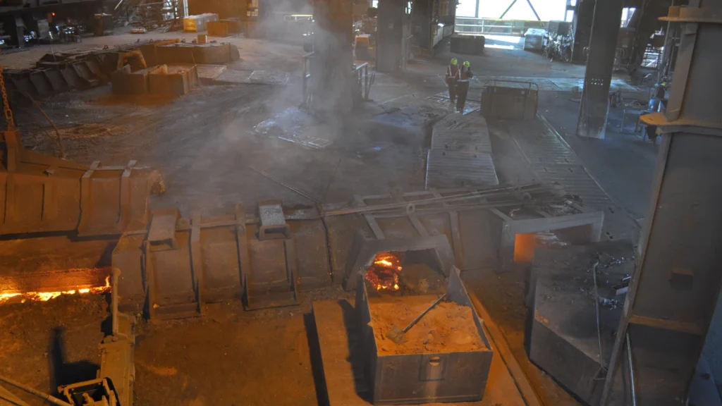 Molten iron glowing in the cast house of the Whyalla ironworks as two workers walk past