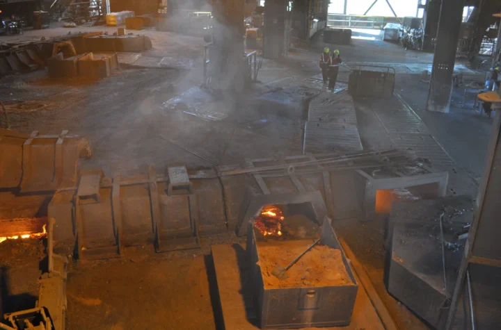 Molten iron glowing in the cast house of the Whyalla ironworks as two workers walk past